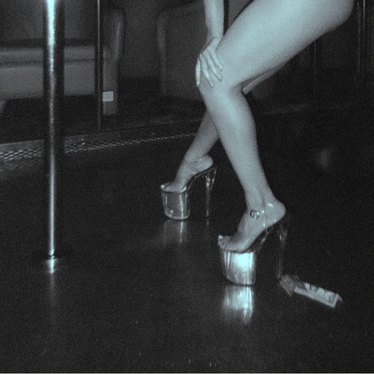 a stripper on stage in platforms next to a pole with dollar bills near her feet